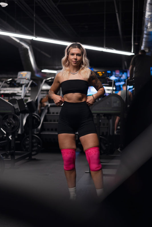 woman posing at the gym wearing neon pink knee sleeves